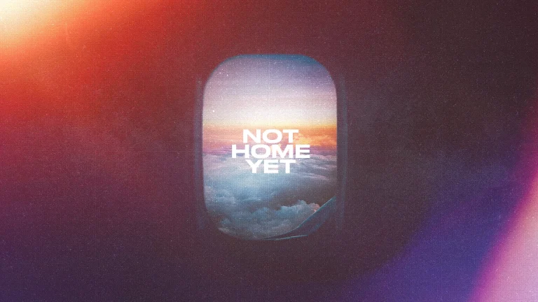Clouds and a colorful sky viewed through an airplane window with the text "NOT HOME YET," symbolizing spiritual journey.