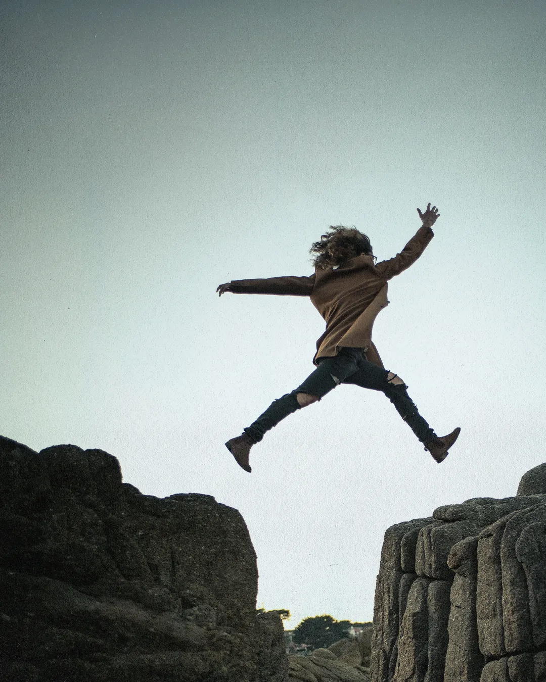 Person leaping between rocks, symbolizing faith, courage, and spiritual journey.