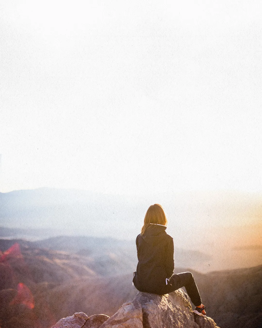 Person sitting on a mountain at sunrise, symbolizing reflection, solitude, and spiritual connection with God's creation.