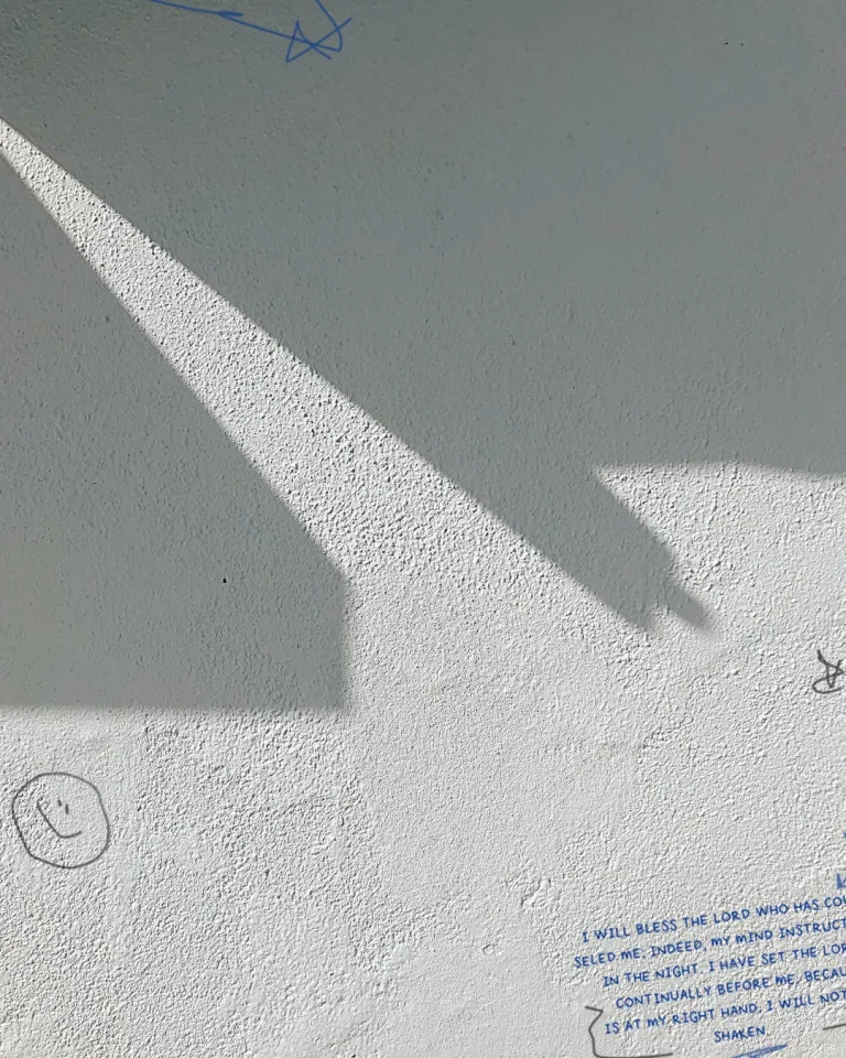 Sunlight casting church-like shadow on a wall with scripture and simple drawings, symbolizing faith and reflection.