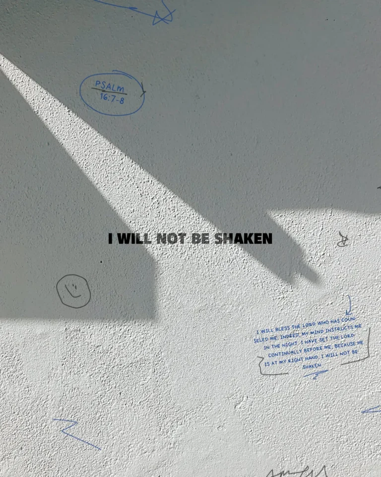 Text on wall says, "I will not be shaken," with Psalm 16:7-8 references and hand-drawn doodles, conveying faith and resilience.