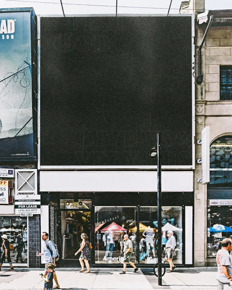 Street scene with people walking, storefront advertising sales, and a large blank billboard above, suggesting potential outreach.
