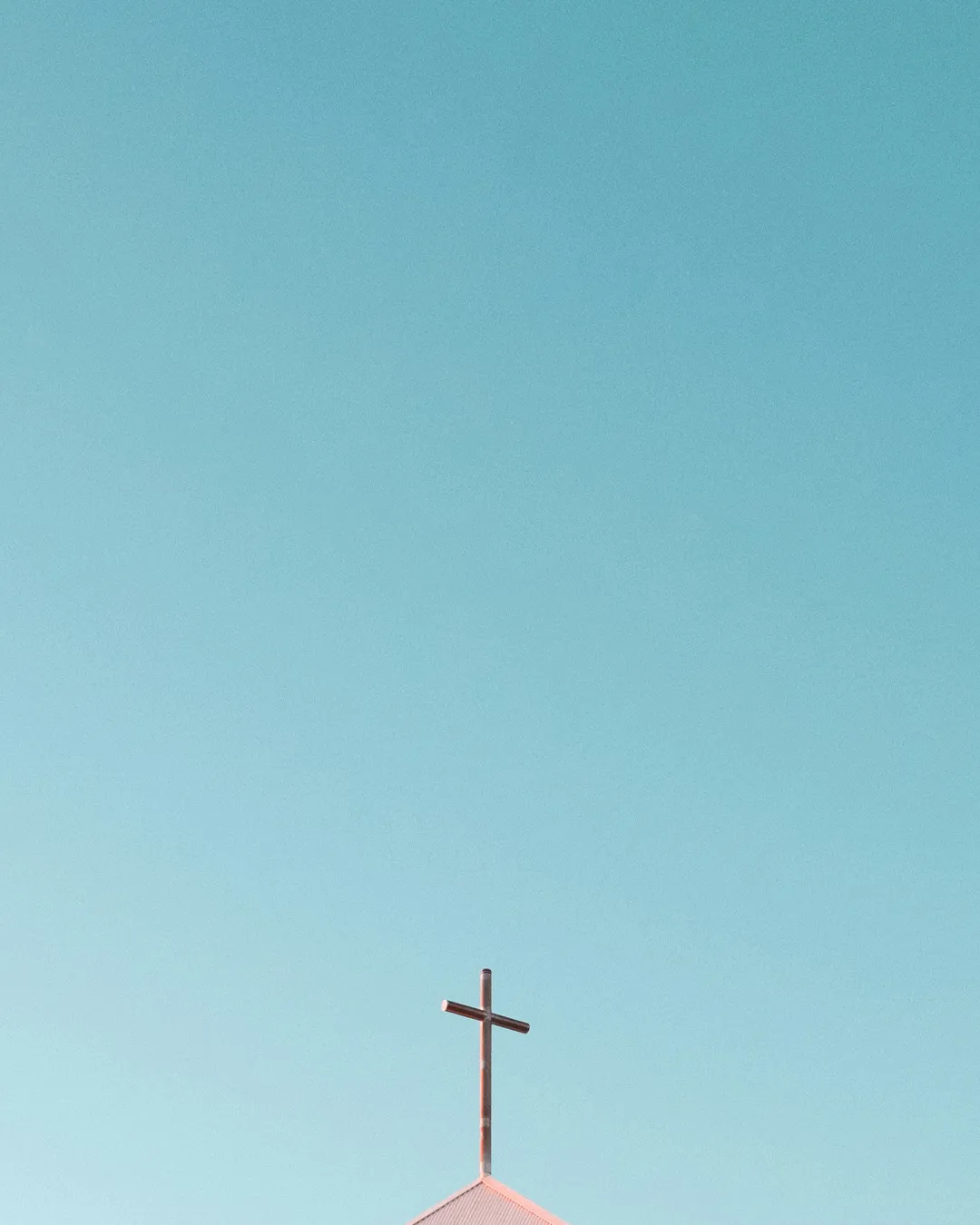 Cross atop a church against a clear blue sky, symbolizing faith, hope, and community in worship.