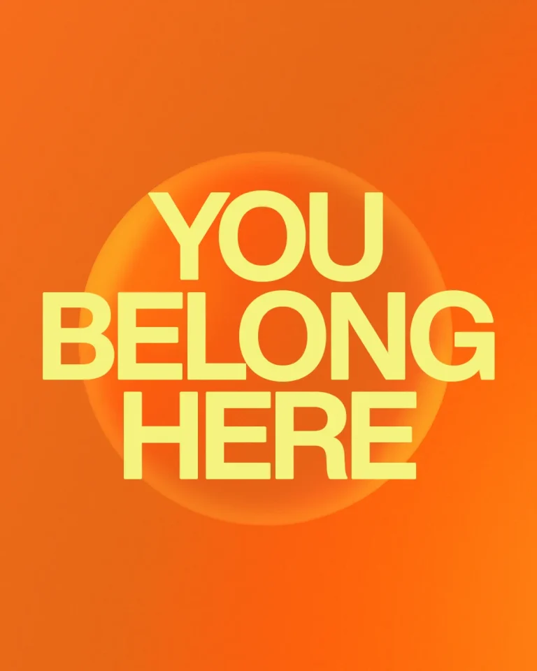 Bright orange background with bold yellow text stating "YOU BELONG HERE," conveying a message of community and inclusion.