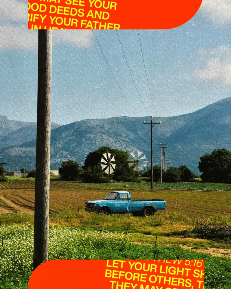 Blue pickup truck parked in a field with mountains and windmills in the background, symbolizing faith and community service.