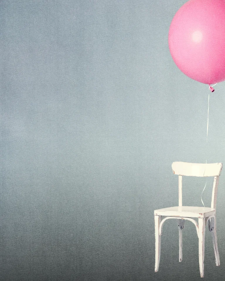 A white chair floats with a pink balloon, symbolizing hope and the uplifting spirit of community and faith.