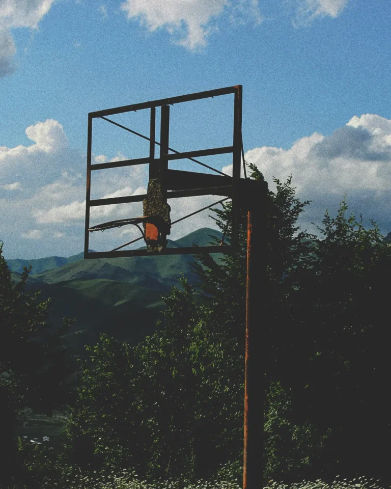 A weathered basketball hoop stands amidst lush greenery and mountains, symbolizing community and fellowship in faith.