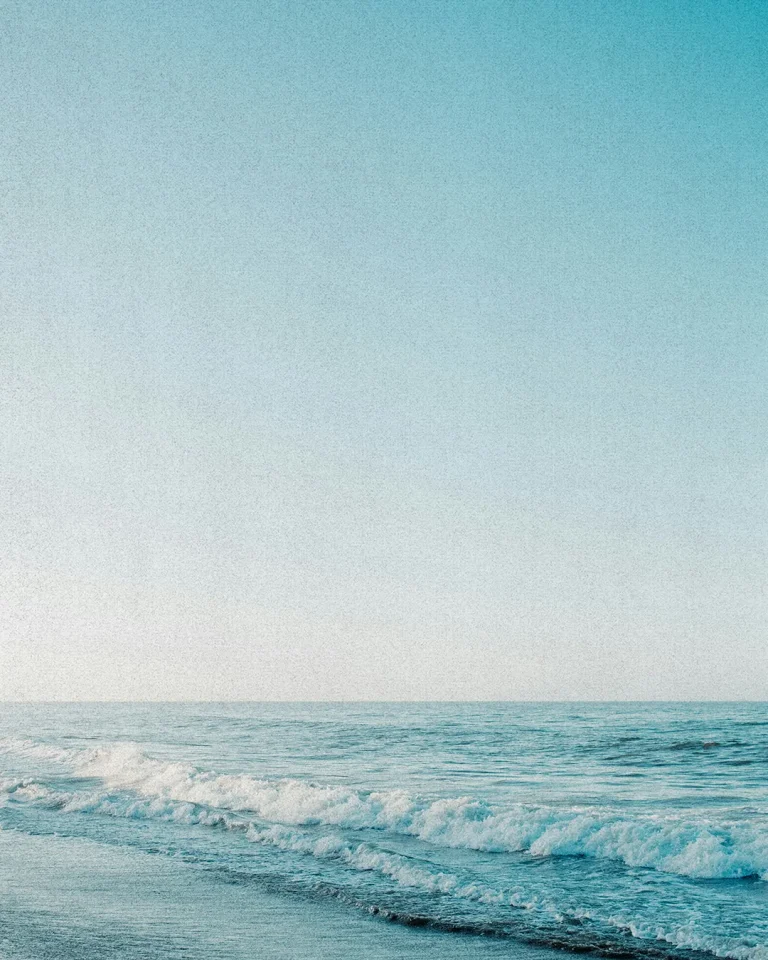 Serene ocean waves gently lapping the shore under a clear blue sky, symbolizing peace and divine creation.