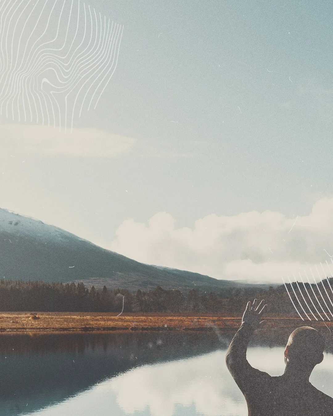 Person worships by a serene lake, raising hands in praise, surrounded by mountains and reflections of nature's beauty.