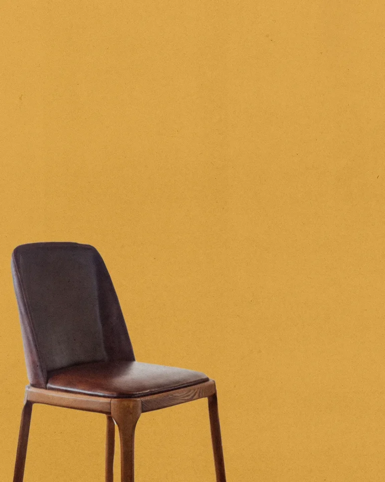 Simple wooden chair against a warm yellow background, symbolizing a welcoming space for worship and community gathering.